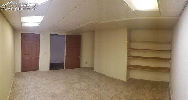 basement featuring a paneled ceiling and light colored carpet