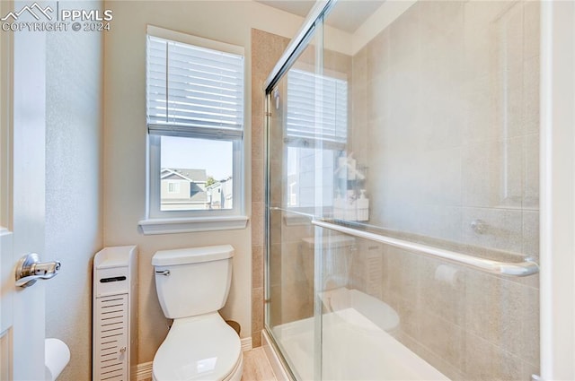 bathroom with toilet, a shower with shower door, and plenty of natural light