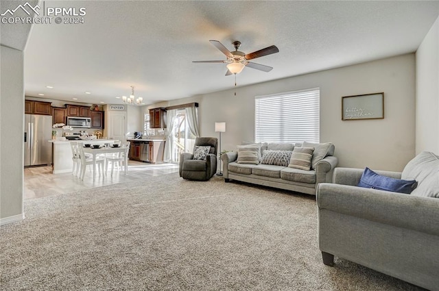 living room with a textured ceiling, ceiling fan with notable chandelier, and light carpet