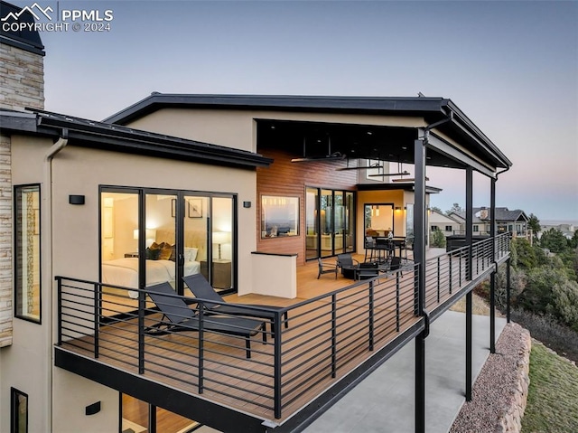 back of property at dusk featuring a balcony and stucco siding