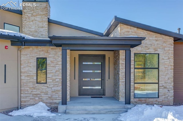 snow covered property entrance with stone siding and stucco siding