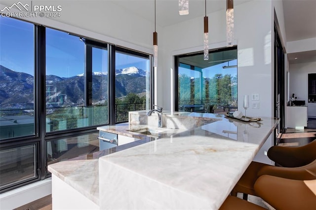 kitchen featuring a kitchen island with sink, a mountain view, a sink, light stone countertops, and a kitchen bar