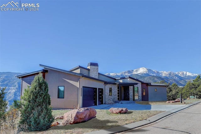 view of front facade featuring an attached garage, a mountain view, stone siding, stucco siding, and a chimney