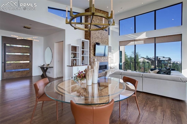 dining area with a towering ceiling, a large fireplace, a notable chandelier, and wood finished floors