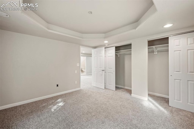 unfurnished bedroom featuring a tray ceiling, two closets, and carpet