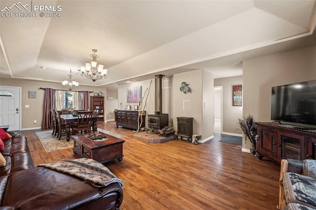 living room featuring hardwood / wood-style floors, a wood stove, a notable chandelier, and a raised ceiling