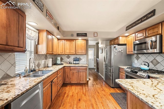 kitchen with stainless steel appliances, light stone counters, decorative backsplash, sink, and light wood-type flooring