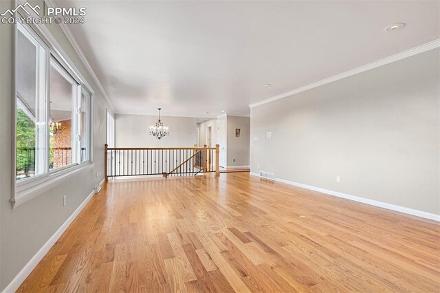 empty room featuring a notable chandelier, crown molding, and light hardwood / wood-style flooring