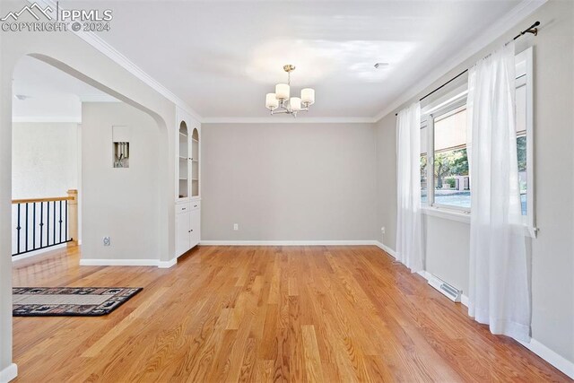 spare room featuring ornamental molding, light hardwood / wood-style flooring, a chandelier, and built in shelves