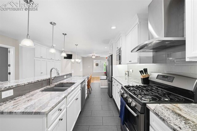 kitchen featuring white cabinetry, wall chimney range hood, appliances with stainless steel finishes, pendant lighting, and sink