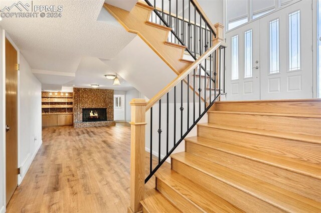 stairway with hardwood / wood-style floors, a textured ceiling, and a brick fireplace