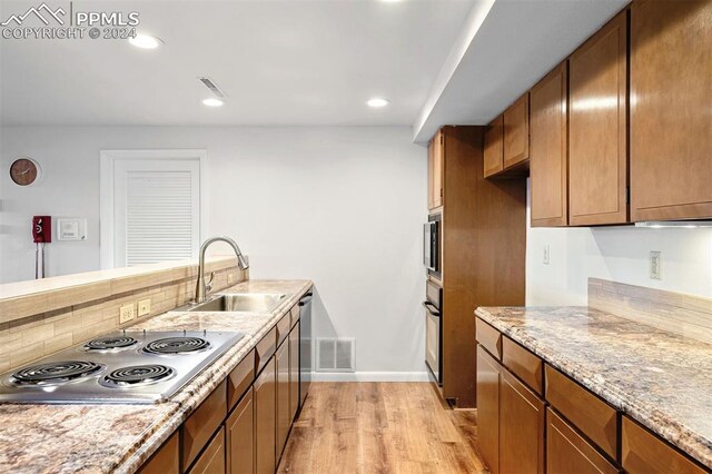 kitchen with stainless steel gas stovetop, sink, tasteful backsplash, light stone countertops, and light wood-type flooring