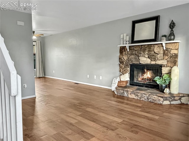 living room with hardwood / wood-style flooring, ceiling fan, and a stone fireplace