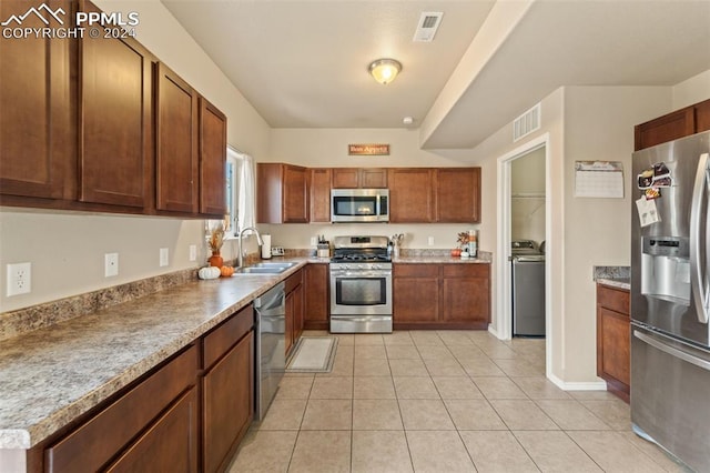 kitchen featuring stainless steel appliances, light tile patterned flooring, sink, and washer / clothes dryer