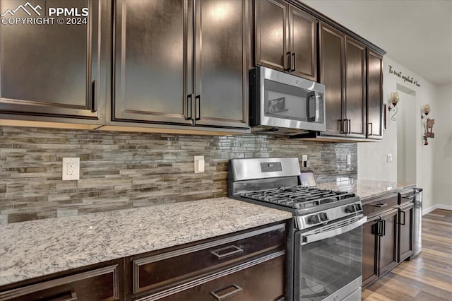 kitchen with stainless steel appliances, light stone countertops, hardwood / wood-style floors, dark brown cabinets, and decorative backsplash