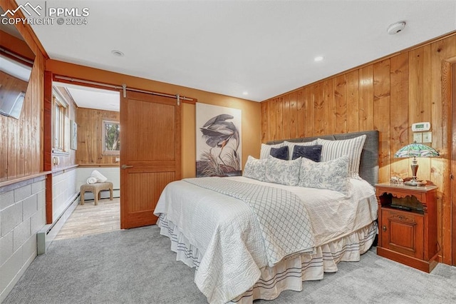 carpeted bedroom featuring a barn door, wood walls, and a baseboard radiator