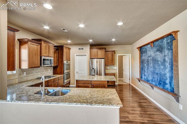 10978 Middlegate Ct, Peyton, CO 80831 - kitchen featuring stainless steel appliances, a sink, brown cabinets, backsplash, and light stone counters