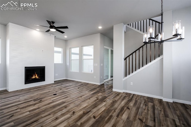 unfurnished living room with a fireplace, ceiling fan with notable chandelier, and dark wood-type flooring