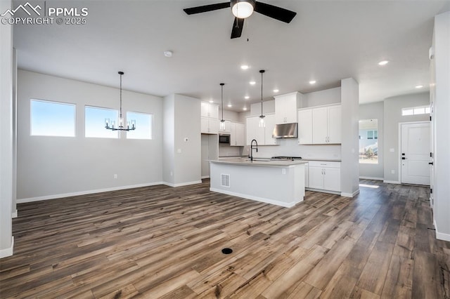 kitchen featuring ceiling fan with notable chandelier, decorative light fixtures, white cabinetry, and an island with sink