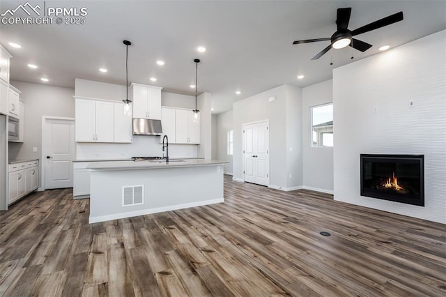 kitchen with white cabinetry, a fireplace, an island with sink, and decorative light fixtures