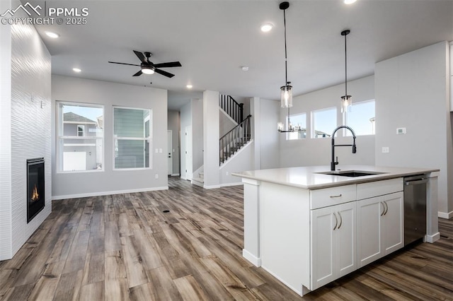 kitchen with white cabinetry, sink, dishwasher, a fireplace, and a center island with sink