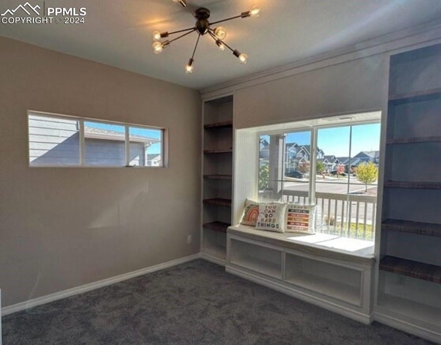 interior space featuring dark colored carpet, a healthy amount of sunlight, built in features, and a chandelier