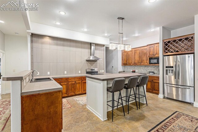 kitchen featuring wall chimney exhaust hood, sink, decorative light fixtures, appliances with stainless steel finishes, and a kitchen island