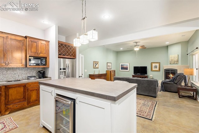 kitchen with a center island, hanging light fixtures, black microwave, stainless steel fridge, and beverage cooler