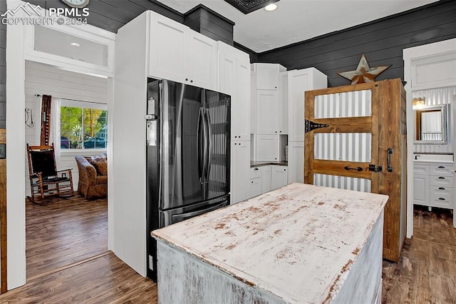 kitchen featuring dark hardwood / wood-style floors, wooden walls, stainless steel fridge, and white cabinets