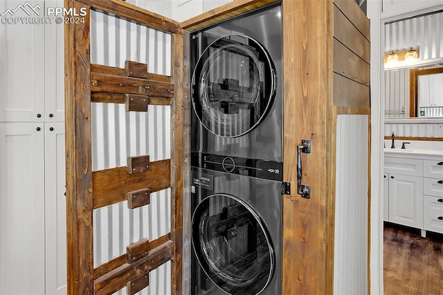 clothes washing area featuring stacked washer and clothes dryer, dark hardwood / wood-style floors, and sink