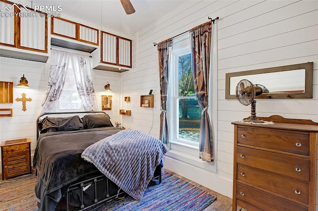 bedroom with light wood-type flooring, wooden walls, and ceiling fan