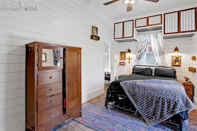 bedroom with hardwood / wood-style flooring, ceiling fan, and wooden walls