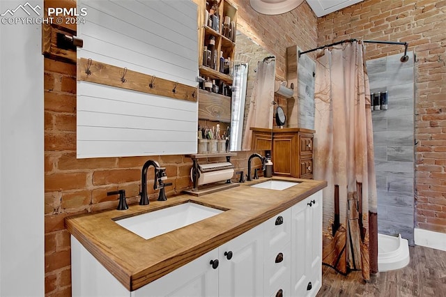 bathroom featuring vanity, hardwood / wood-style floors, a shower with shower curtain, and brick wall