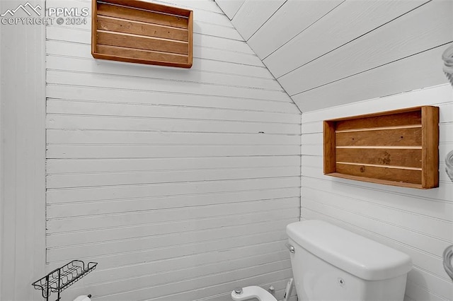 bathroom featuring wooden walls, toilet, and lofted ceiling