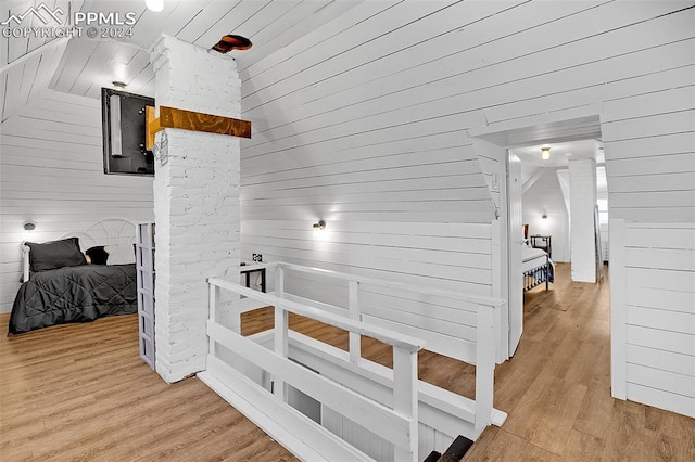 hall with wooden walls, light wood-type flooring, and lofted ceiling