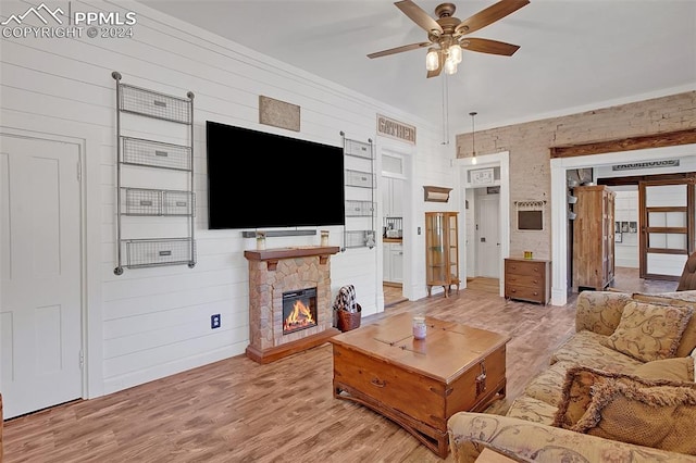 living room with hardwood / wood-style floors, ceiling fan, wood walls, and a stone fireplace