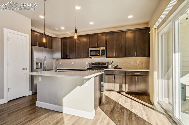 kitchen with appliances with stainless steel finishes, a kitchen island with sink, sink, light hardwood / wood-style flooring, and hanging light fixtures