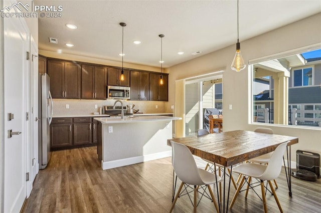 kitchen with dark hardwood / wood-style floors, pendant lighting, decorative backsplash, dark brown cabinets, and appliances with stainless steel finishes