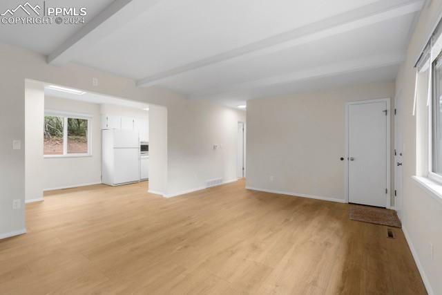 empty room featuring light wood-type flooring and beamed ceiling