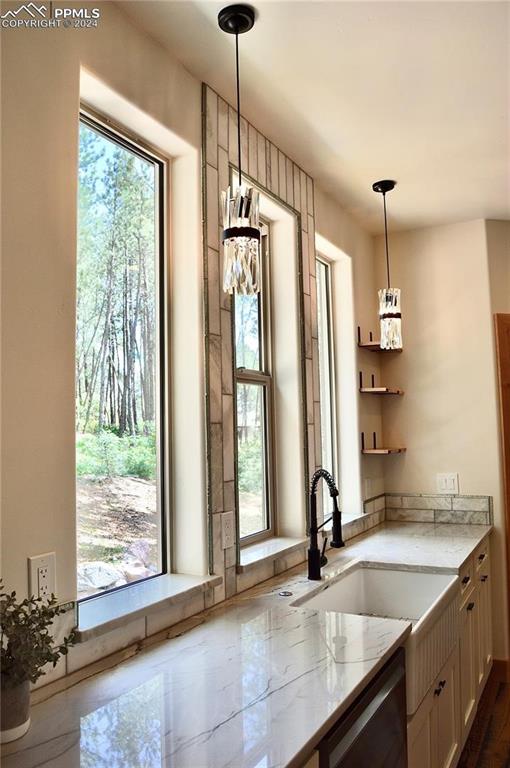 kitchen featuring sink, stainless steel dishwasher, decorative light fixtures, and light stone counters