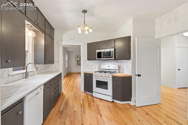 kitchen with tasteful backsplash, white appliances, light hardwood / wood-style floors, and hanging light fixtures