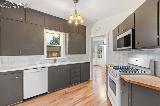 kitchen with tasteful backsplash, hanging light fixtures, sink, white appliances, and light hardwood / wood-style flooring