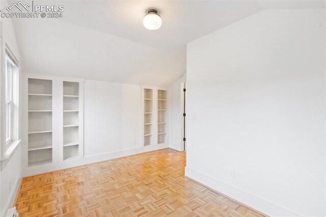 spare room with a baseboard heating unit, built in shelves, lofted ceiling, and light parquet floors