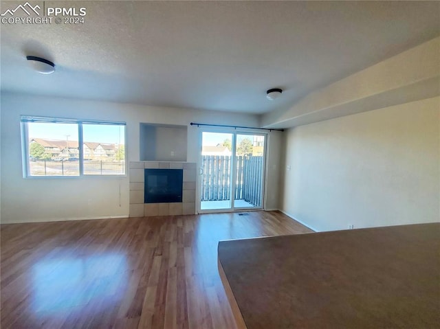 unfurnished living room featuring hardwood / wood-style flooring, plenty of natural light, a textured ceiling, and a tile fireplace