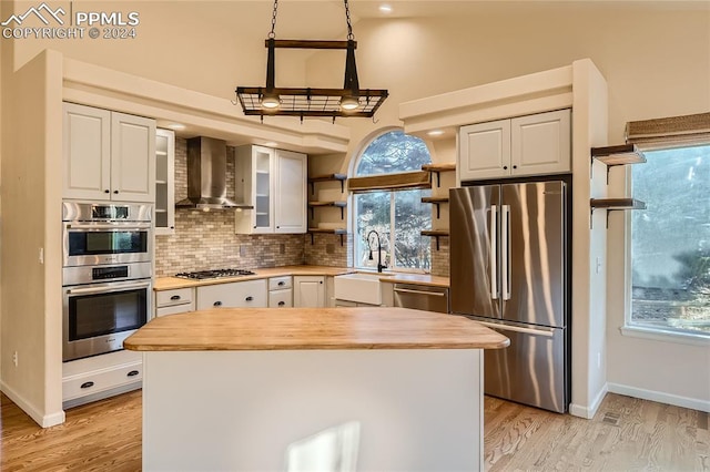 kitchen featuring stainless steel appliances, wall chimney exhaust hood, white cabinets, and wood counters