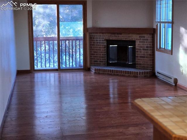 unfurnished living room with hardwood / wood-style flooring, a brick fireplace, and a baseboard heating unit