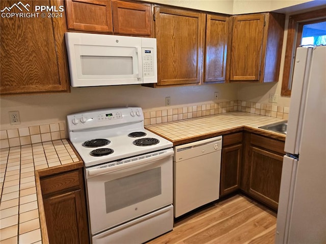 kitchen featuring tile counters, white appliances, and light wood-type flooring