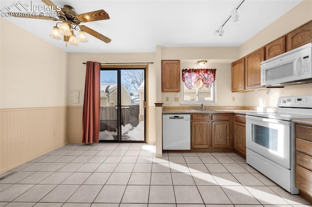 kitchen featuring light tile patterned flooring, sink, ceiling fan, white appliances, and wooden walls