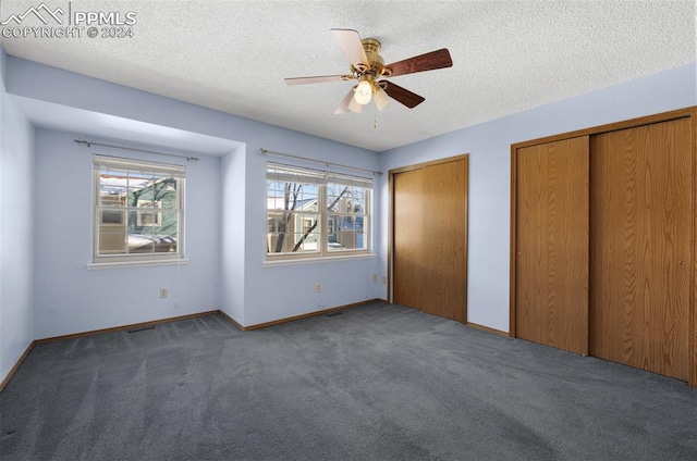 unfurnished bedroom with multiple closets, a textured ceiling, dark colored carpet, and ceiling fan