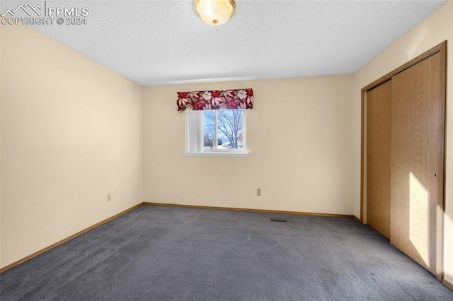 unfurnished room with a textured ceiling and dark carpet